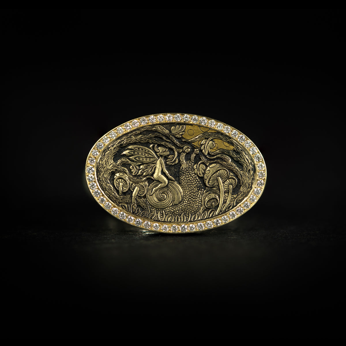 Hand engraved bas-relief fantasy signet ring. Features a fairy riding a snail amongst trees and mushrooms under the moon. 9 carat yellow gold top with diamonds and silver band. On black background face on.