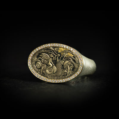 Hand engraved bas-relief fantasy signet ring. Features a fairy riding a snail amongst trees and mushrooms under the moon. 9 carat yellow gold top with diamonds and silver band. On black background side on.