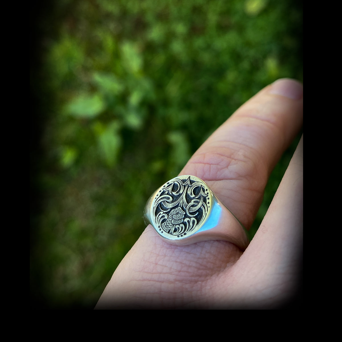 Silver oval jewellery signet ring hand engraved with fantasy scene of Poseidon thrusting his trident from the water. On finger for scale