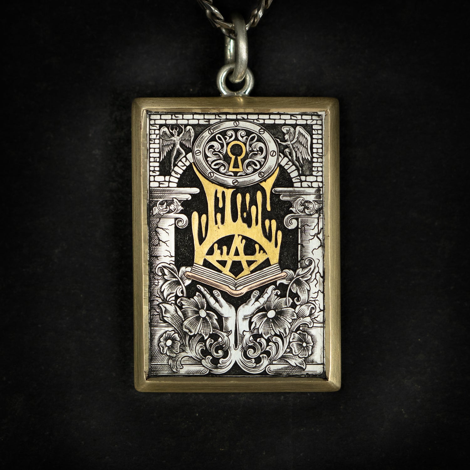 Hand engraved jewellery pendant featuring hands holding a book with a pentacle dripping upwards. It's surrounded by ornamental design including flowers, pillars and angels. Steel, silver and yellow gold