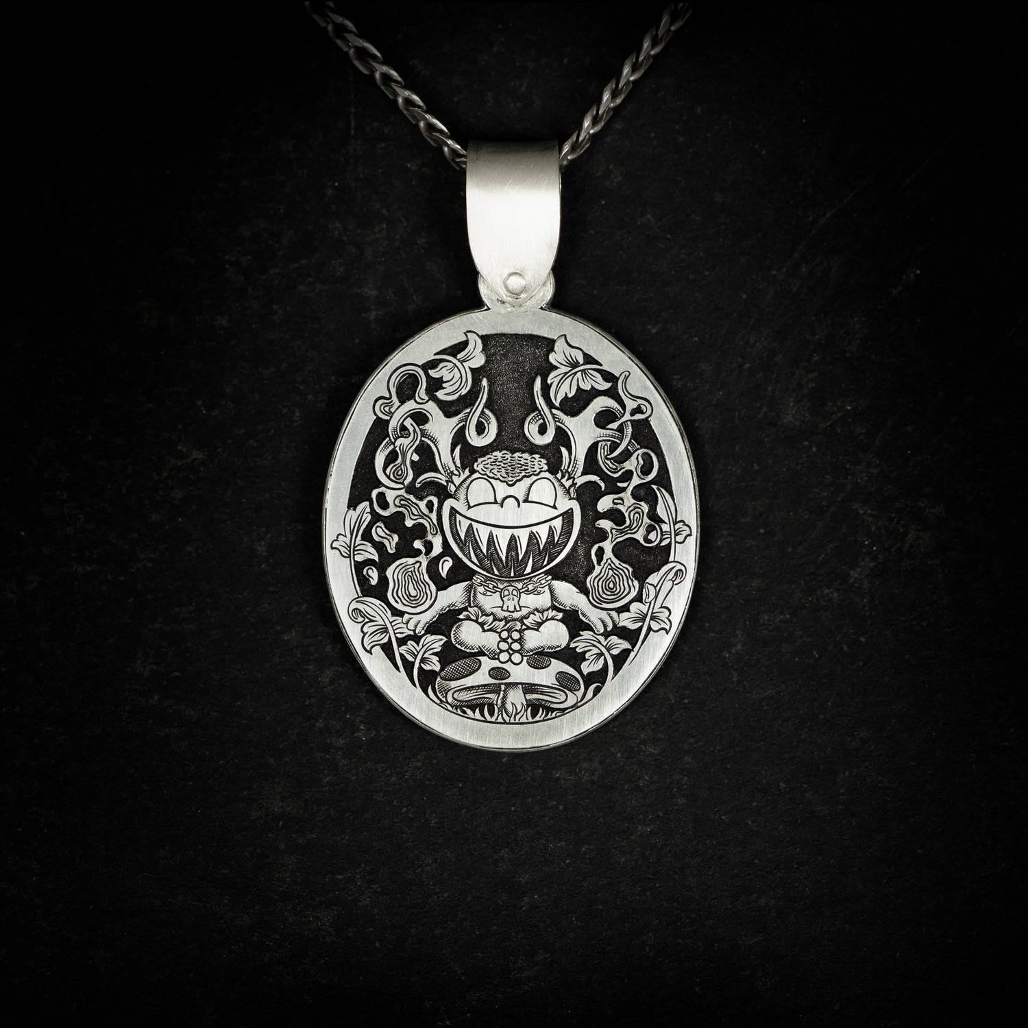 Hand engraved silver jewellery pendant featuring a fantasy cartoon style engraving with a child like creature with antlers, sitting on a mushroom wielding magic. On black background