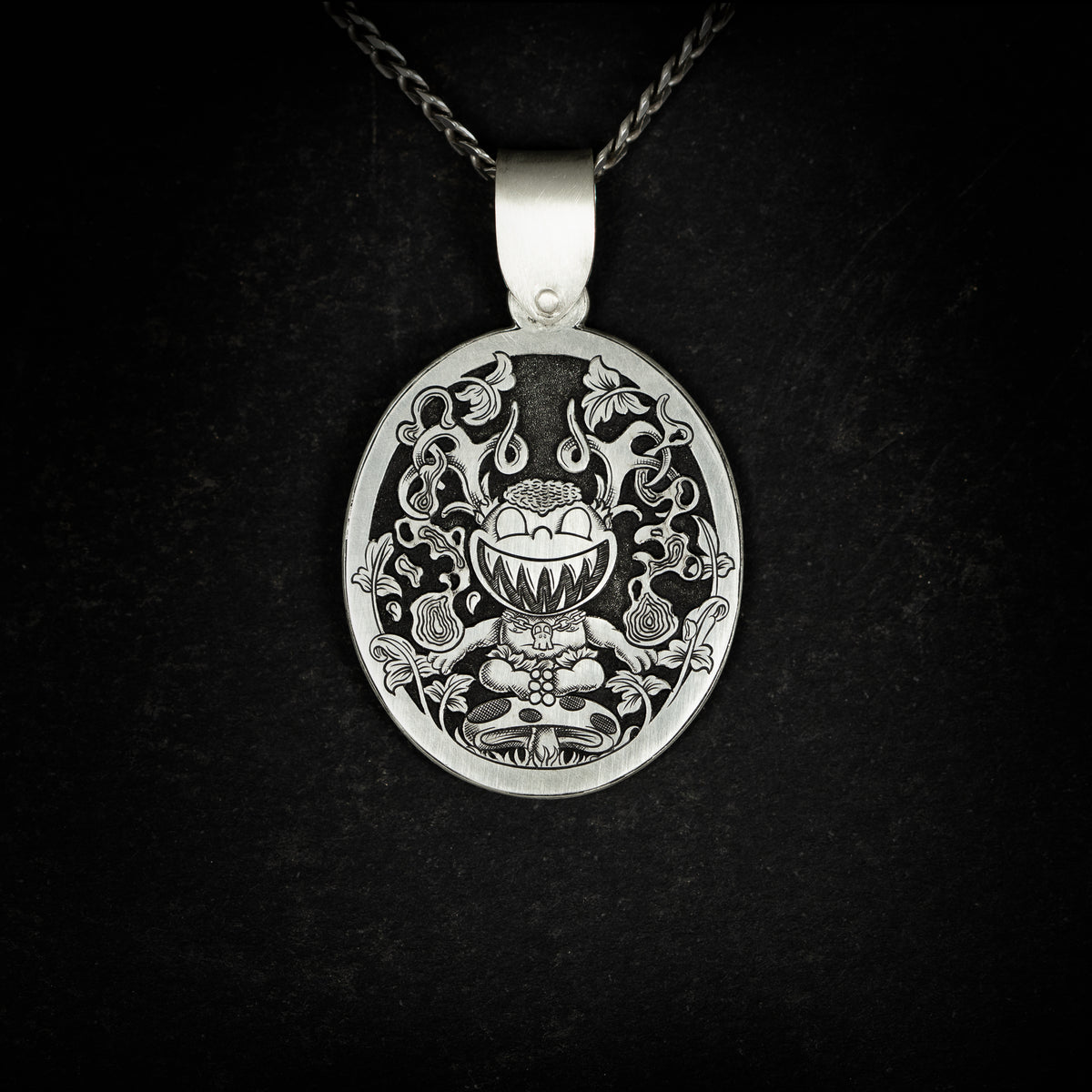 Hand engraved silver jewellery pendant featuring a fantasy cartoon style engraving with a child like creature with antlers, sitting on a mushroom wielding magic. On black background