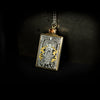 Hand engraved jewellery pendant featuring fantasy scene of a mage deity worshipped in a temple. Made from steel, 24 carat fine gold, 9 carat yellow gold and silver. Set with an orange zircon gemstone. Displayed on black background on angle
