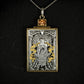 Hand engraved jewellery pendant featuring fantasy scene of a mage deity worshipped in a temple. Made from steel, 24 carat fine gold, 9 carat yellow gold and silver. Set with an orange zircon gemstone. Displayed on black background.