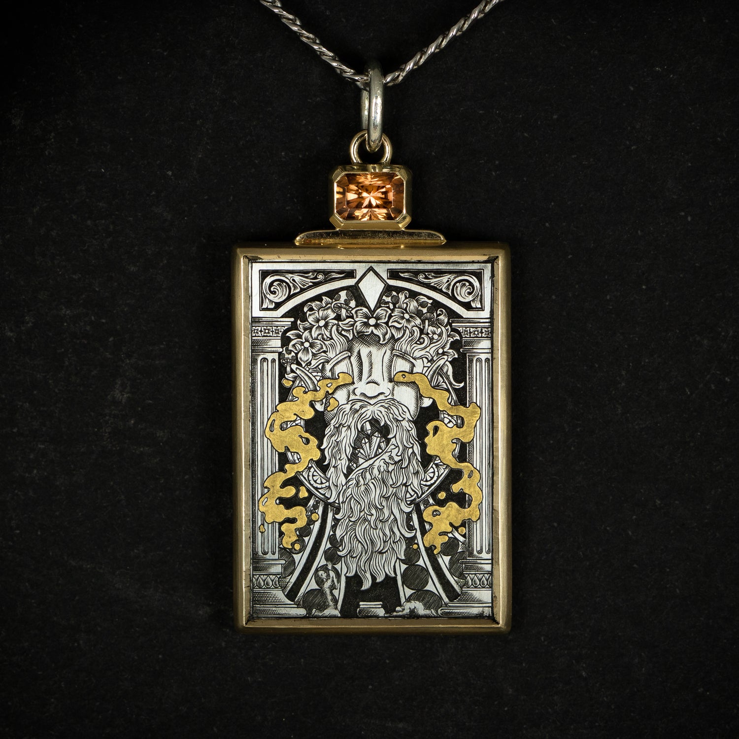 Hand engraved jewellery pendant featuring fantasy scene of a mage deity worshipped in a temple. Made from steel, 24 carat fine gold, 9 carat yellow gold and silver. Set with an orange zircon gemstone. Displayed on black background.