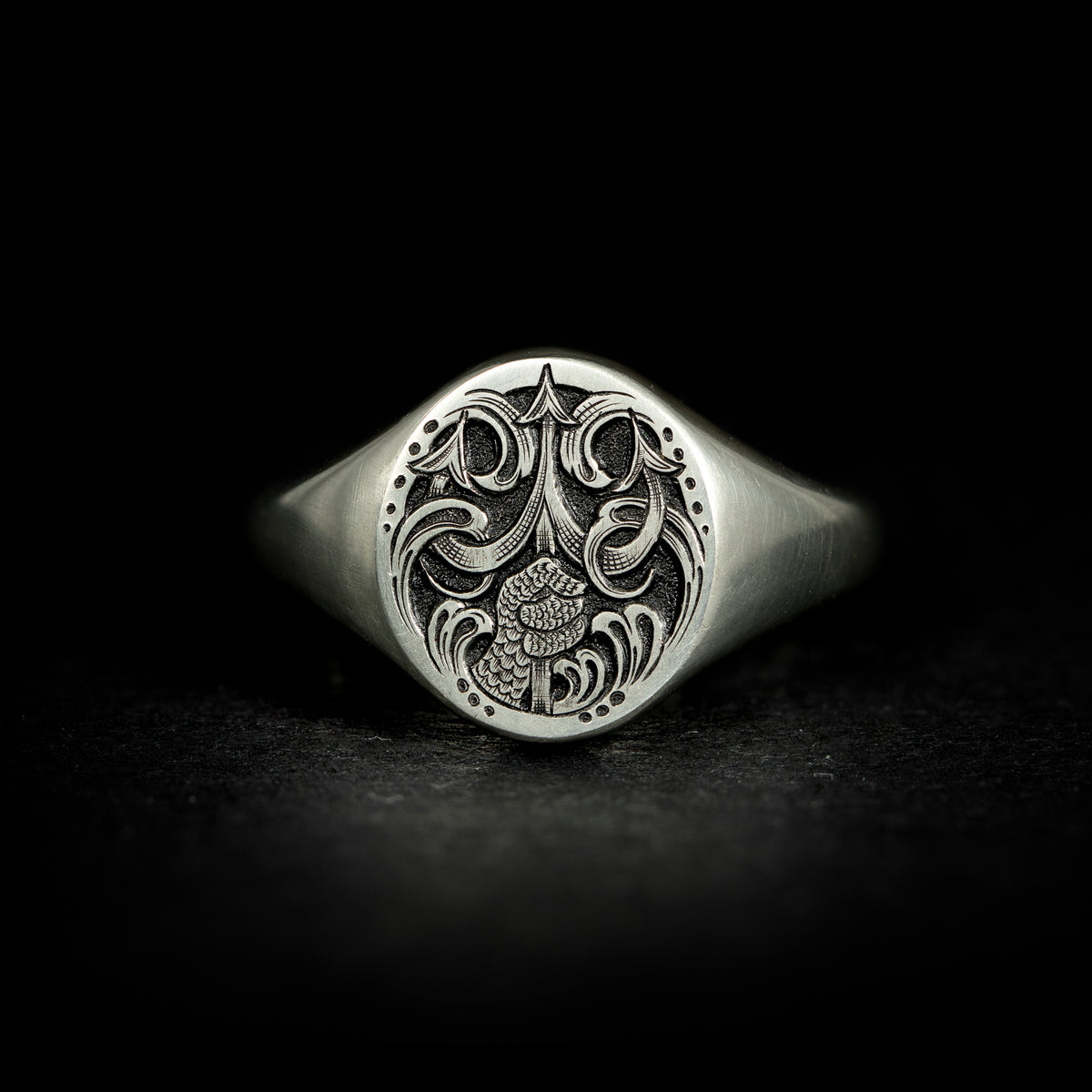Silver oval jewellery signet ring hand engraved with fantasy scene of Poseidon thrusting his trident from the water. On black background face on.