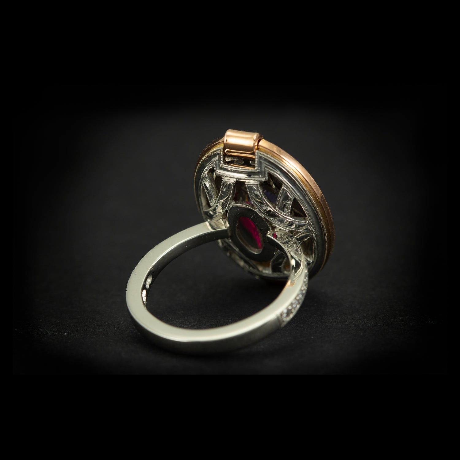 High jewellery, hand made dress ring featuring purple sapphire, rubies and diamonds. Made in platinum, 18 carat rose gold and fine gold. Reverse shot of under ring on black background. 